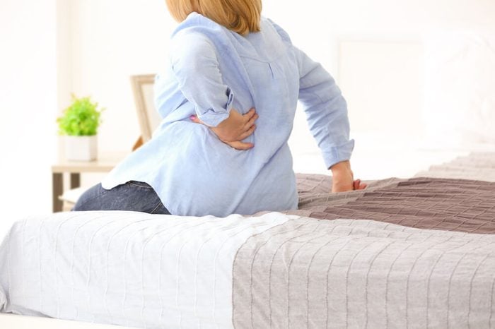Woman suffering from backache at home.