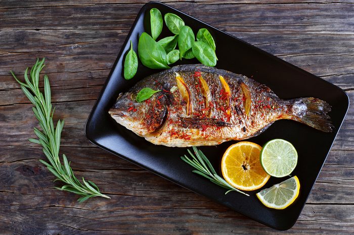 Roast fish with lemon and orange slices, spices, fresh rosemary and spinach 