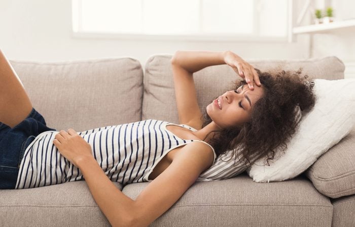 Sad girl with headache lying on sofa at home, copy space