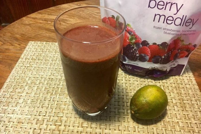 berry colored smoothie with a lime and a berry medley package in the background