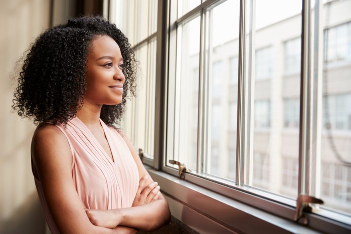 Young black woman with arms crossed looking out of window