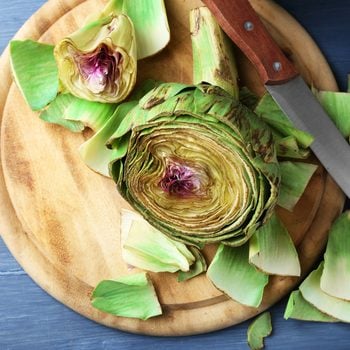 Artichokes on cutting board, on color wooden background