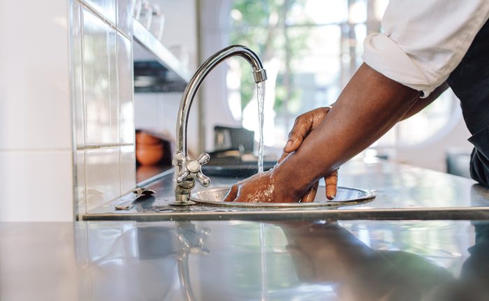 Close up of chef washing his hands in commercial kitchen. Man washing hands in a sink with tap water.