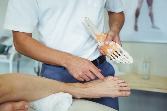 doctor with anatomical foot model and patient's foot