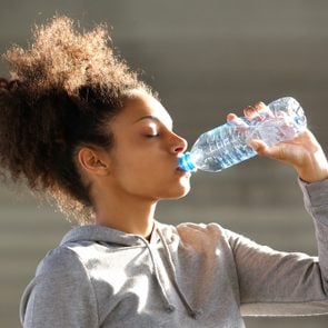 Close up portrait of an attractive young woman drinking water from bottle