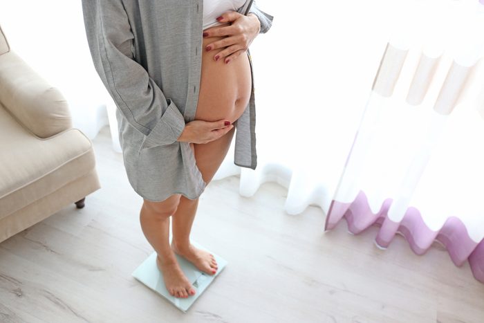 Pregnant woman standing on scales at home