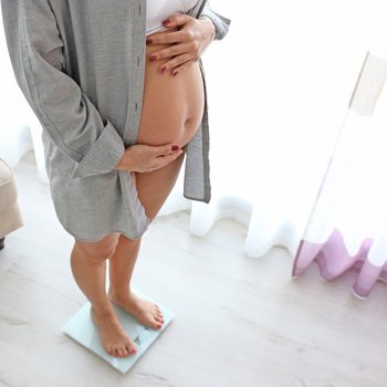 Pregnant woman standing on scales at home