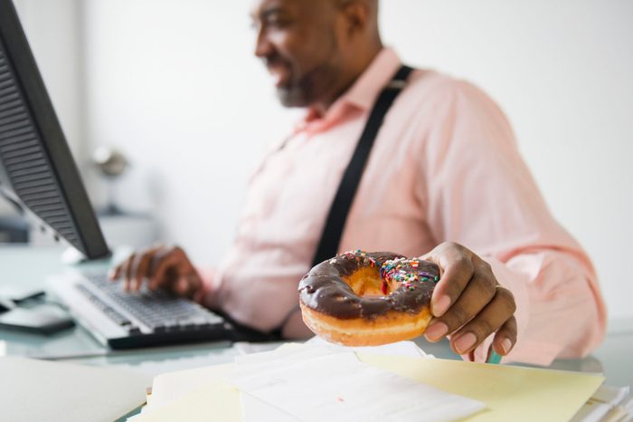 man eating a donut while sitting at desk working