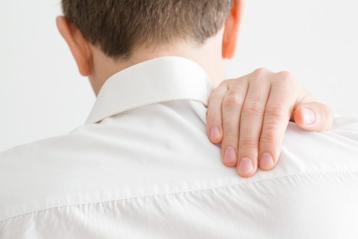 rear view of man holding shoulder from pain