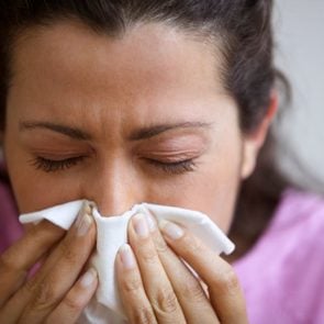 close up of woman blowing nose into tissue