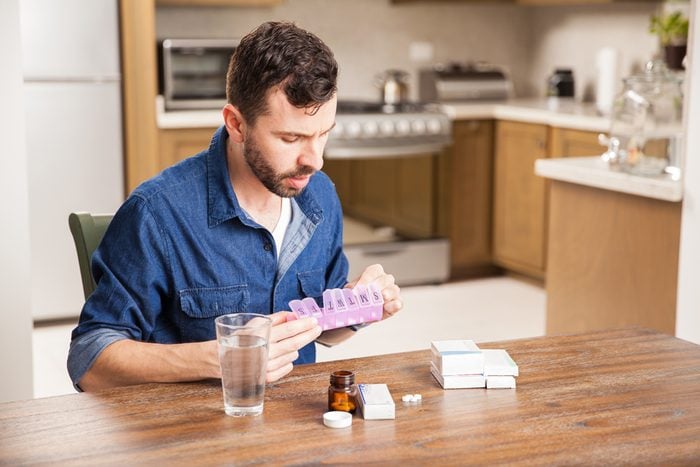 Young man with a beard sorting his medicines in a pill organizer at home