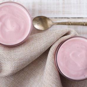 strawberry yogurt in glass with vintage spoon and cloth place on white wooden background. pink yogurt. pink yoghurt, strawberry yoghurt.
