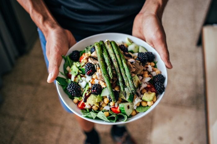 Man holding plate full of vegetarian salad with vegetables and fruits, and berries