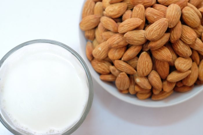 Almond milk in glass with almonds on white background 