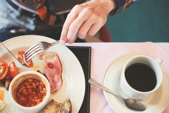 woman eating an English breakfast (beans, ham, tomatoes) and coffee