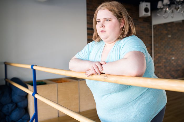 Waist up portrait of obese young woman standing at bar in dance class looking pensively at window