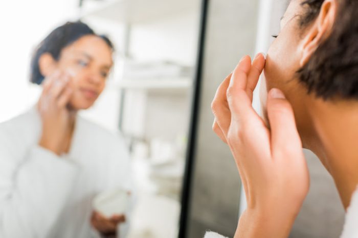 selective focus of african american woman applying cosmetic cream on face in bathroom