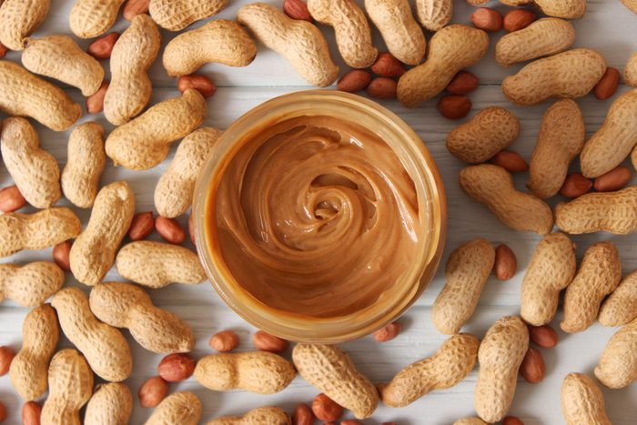 creamy peanut butter in a glass jar and peanut beans on wooden background top view