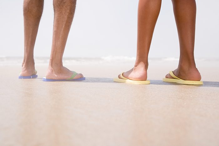 Two people standing on a beach, wearing flip-flops
