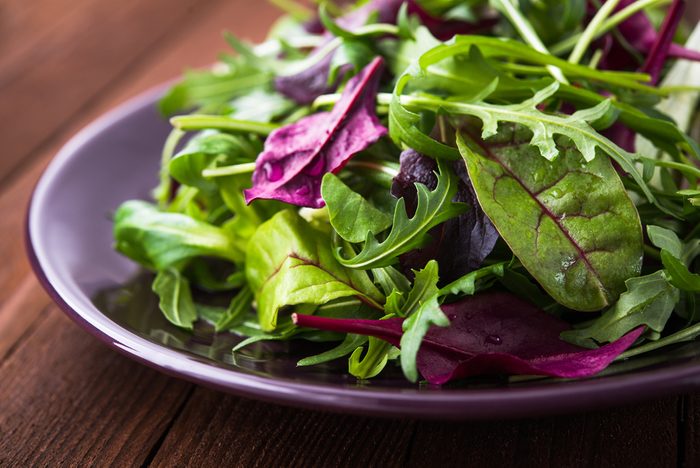 Fresh salad with mixed greens (arugula, mesclun, mache) on dark wooden background close up. Healthy food.