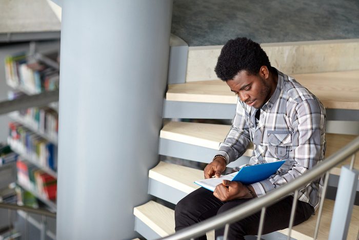 male college student reading on steps