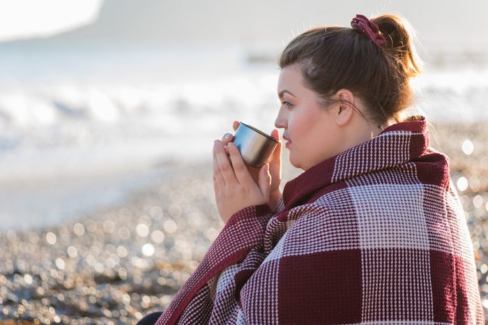 Young plus size woman resting and drinking tea on the beach. 