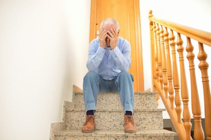 Senior man sitting on the stairs of home with his head in his hands