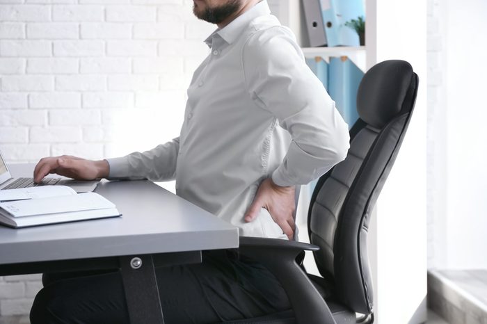 Man suffering from back pain while working with laptop at office