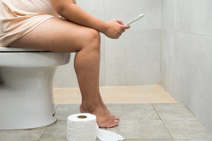 Overweight woman sitting on the toilet and using a tablet