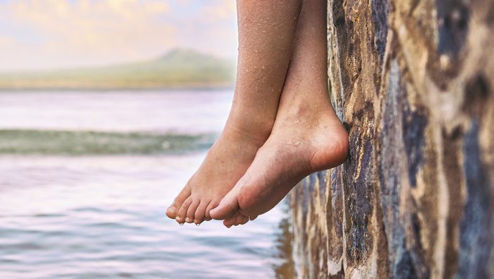 child's wet bare feet dangling from a pier over the water