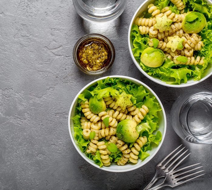 Two bowls of vegetarian healthy salad with macaroni pasta and pesto, avocado balls