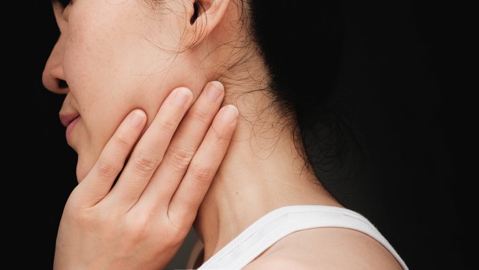 woman with cheek pain or chin pain.Acute pain in a woman Salivary gland . Female holding hand to spot of nape-aches. Concept photo with read spot indicating location of the pain.