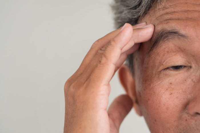 elderly Asian man with hand to his forehead looking confused
