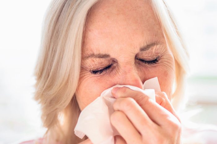 elderly woman pressing a tissue to her face and coughing