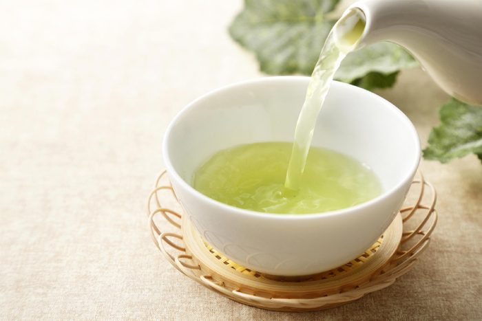 teapot pouring green tea into a ceramic tea bowl