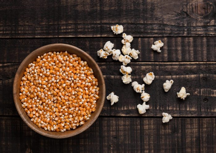 Wooden bowl with raw sweet corn and popcorn on wooden background