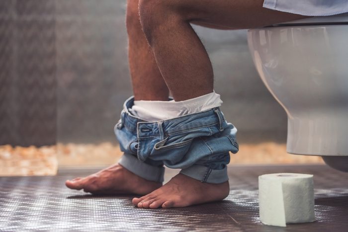 Cropped image of handsome Afro American man sitting on toilet. His jeans is hanging on his legs