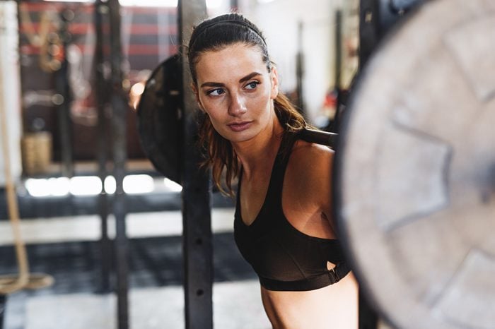 woman at barbell rack with bar on shoulders