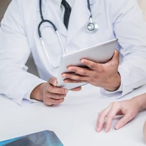 Checking medical tests. Serious doctor and patient. Doctor holding tablet and talking with a patient in the hospital. Close-up view of the hands and the tablet.