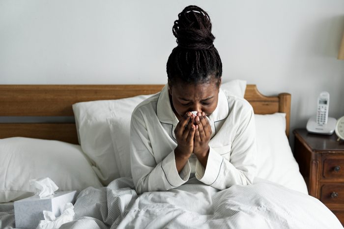 Sick woman in bed blowing her nose, surrounded by tissues