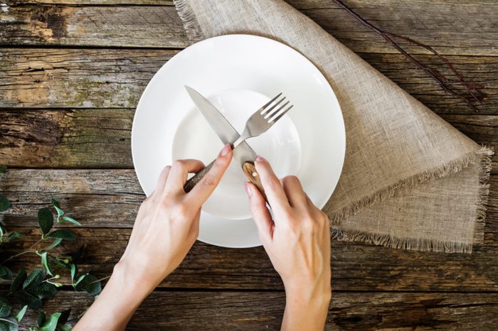 hands holding knife and fork on a plate, top view
