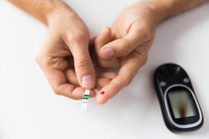 Person with diabetes using a test strip to check his blood sugar level by glucometer at home.