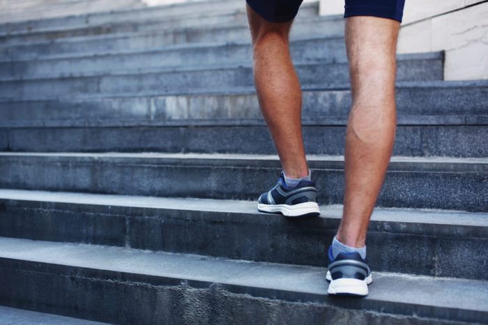 man running in the city, feet of male runner on steps of stairs closeup over urban background