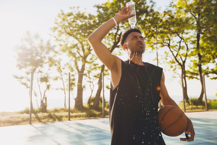 young man spilling water on himself after training, basketball game, tired player, hot summer day