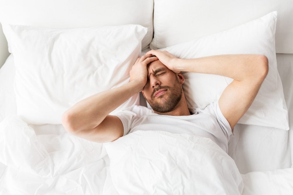 man lying in bed suffering from headache or hangover