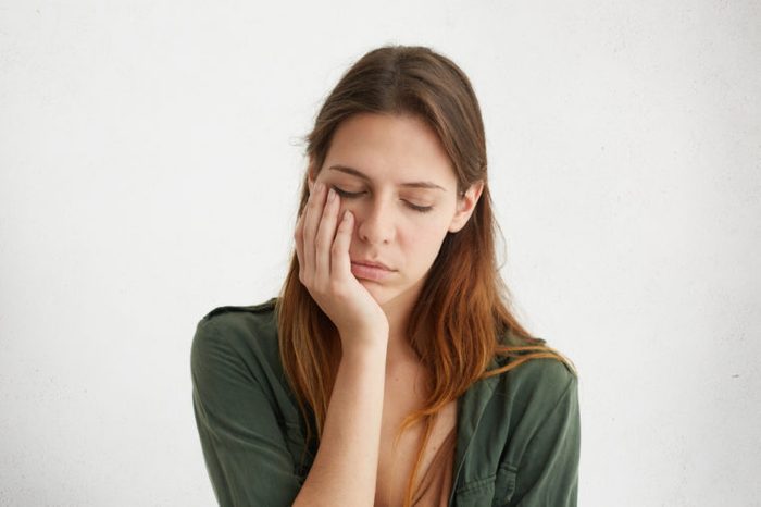 Cute woman looking tired, holding her hand on cheek. closing her eyes with tiredness. Young woman having sad expression and toothache. People, problems, tiredness concept