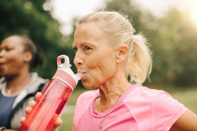 woman drinking water from water bottle outside while exercising