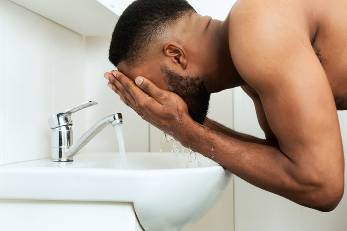 side view of man washing face in bathroom sink