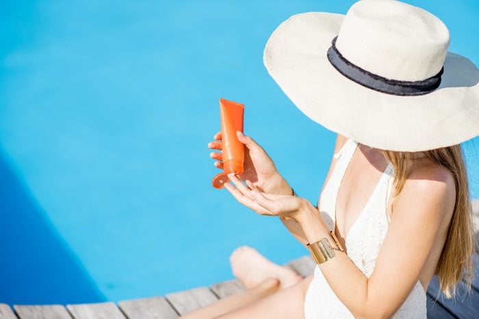 woman in sunhat applying sunscreen by the water