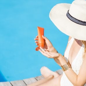 Young beautiful woman applying sunscreen lotion sitting on the wooden poolside. Sunscreen solar cream uv protection concept